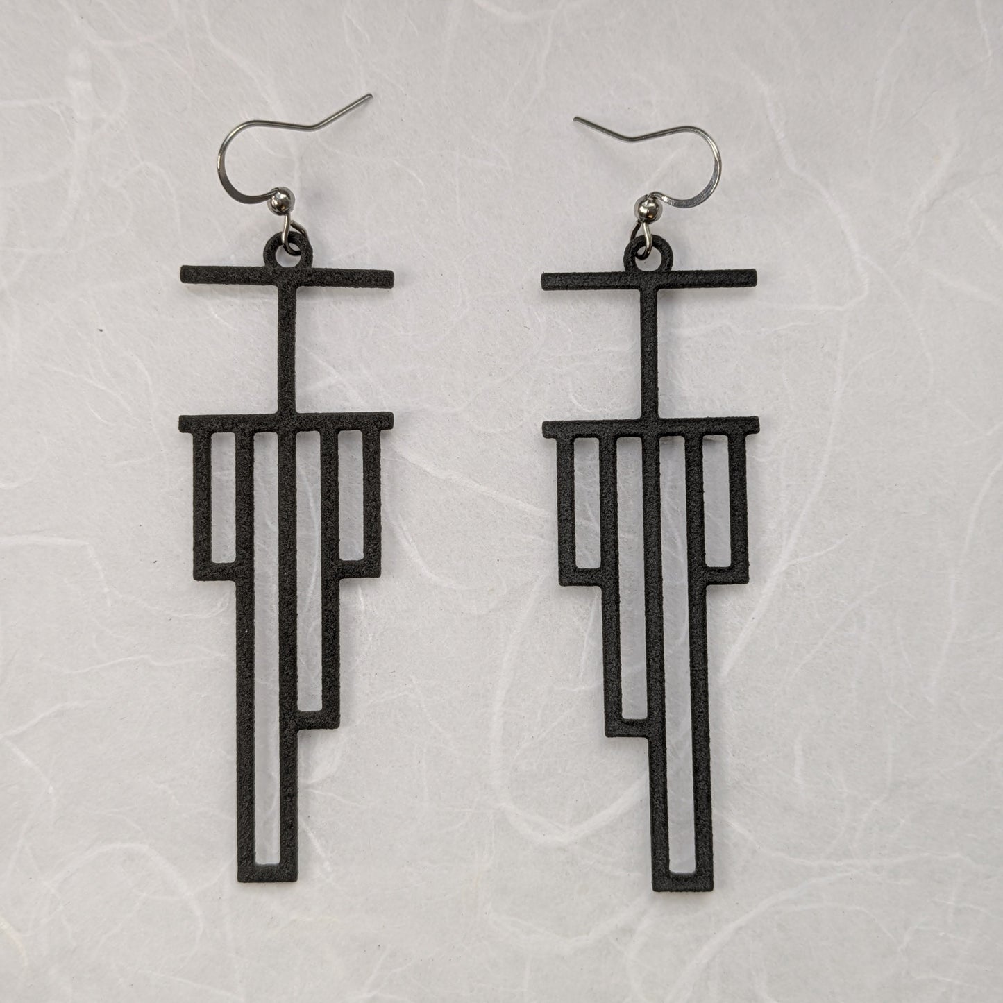 Black geometric earrings on a light gray textured background