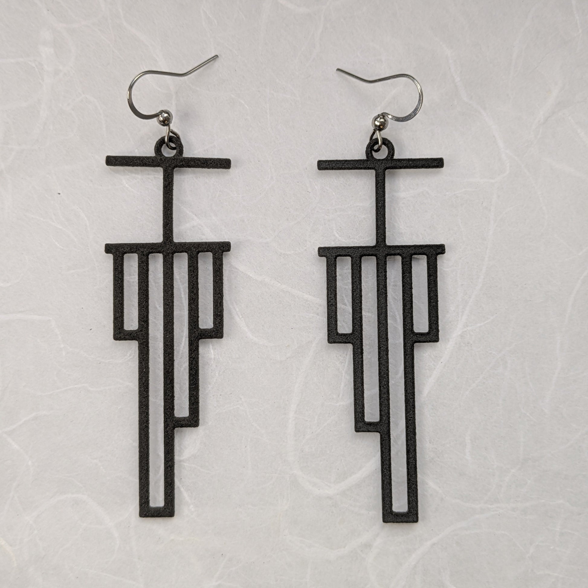 Black geometric earrings on a light gray textured background