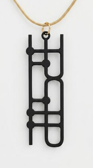 Black geometric pendant on a gold chain against a white background
